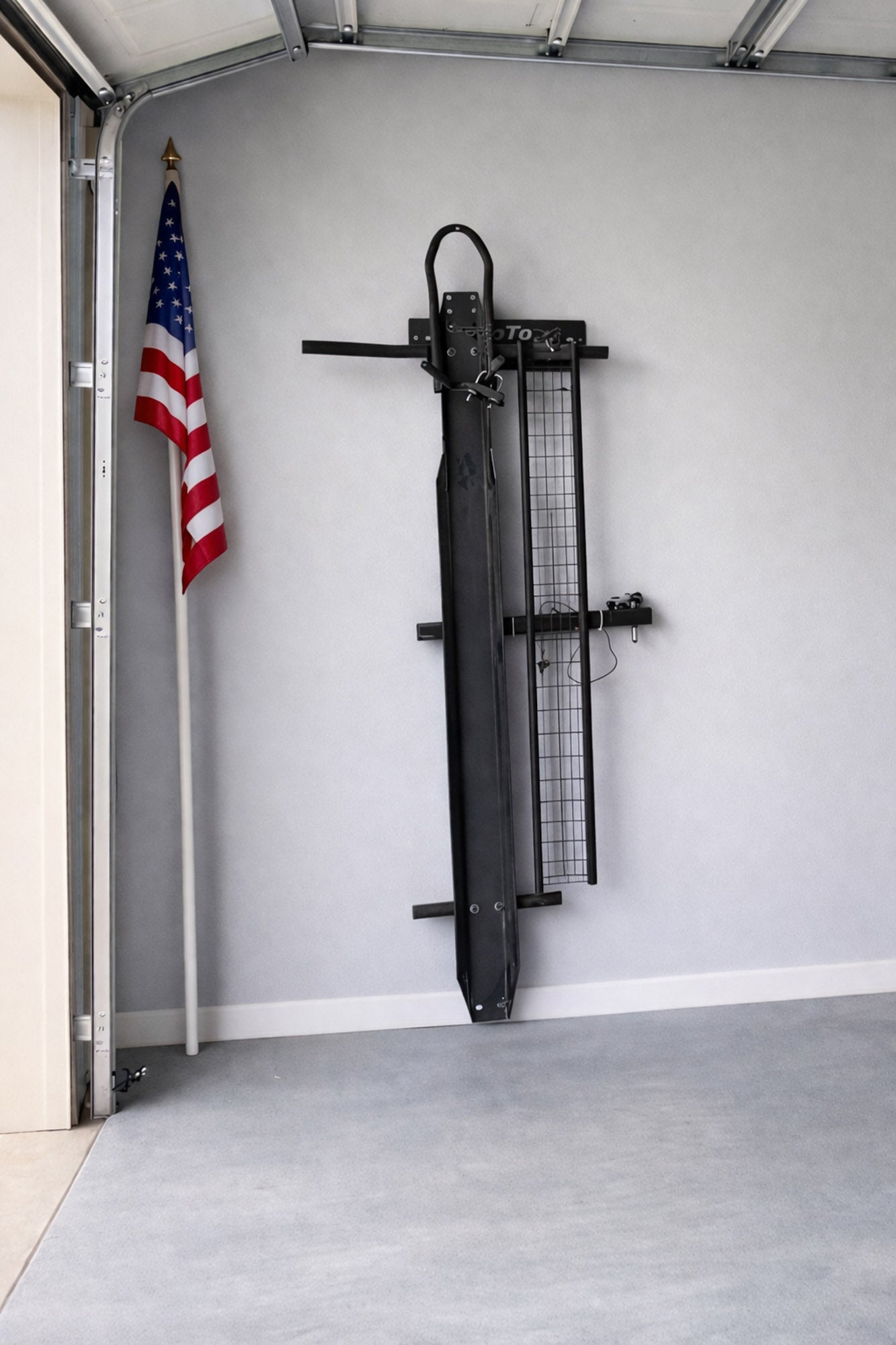 MotoMount wall storage rack holding a MotoTote M3 motorcycle carrier in a garage beside an American flag, showcasing safe and organized motorcycle carrier storage.