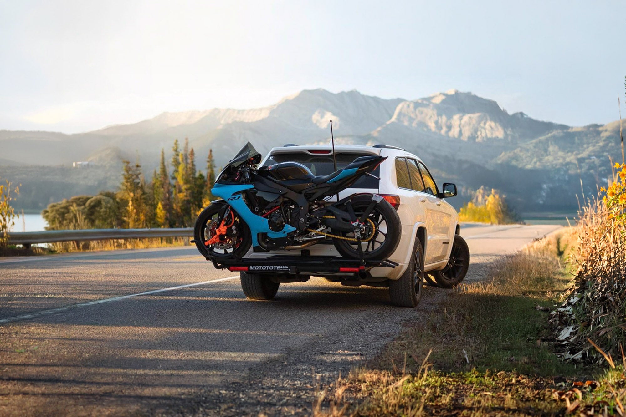 Blue Yamaha R9 mounted on a MotoTote Sport motorcycle carrier attached to a Jeep Grand Cherokee in a scenic mountain landscape during a road trip adventure.