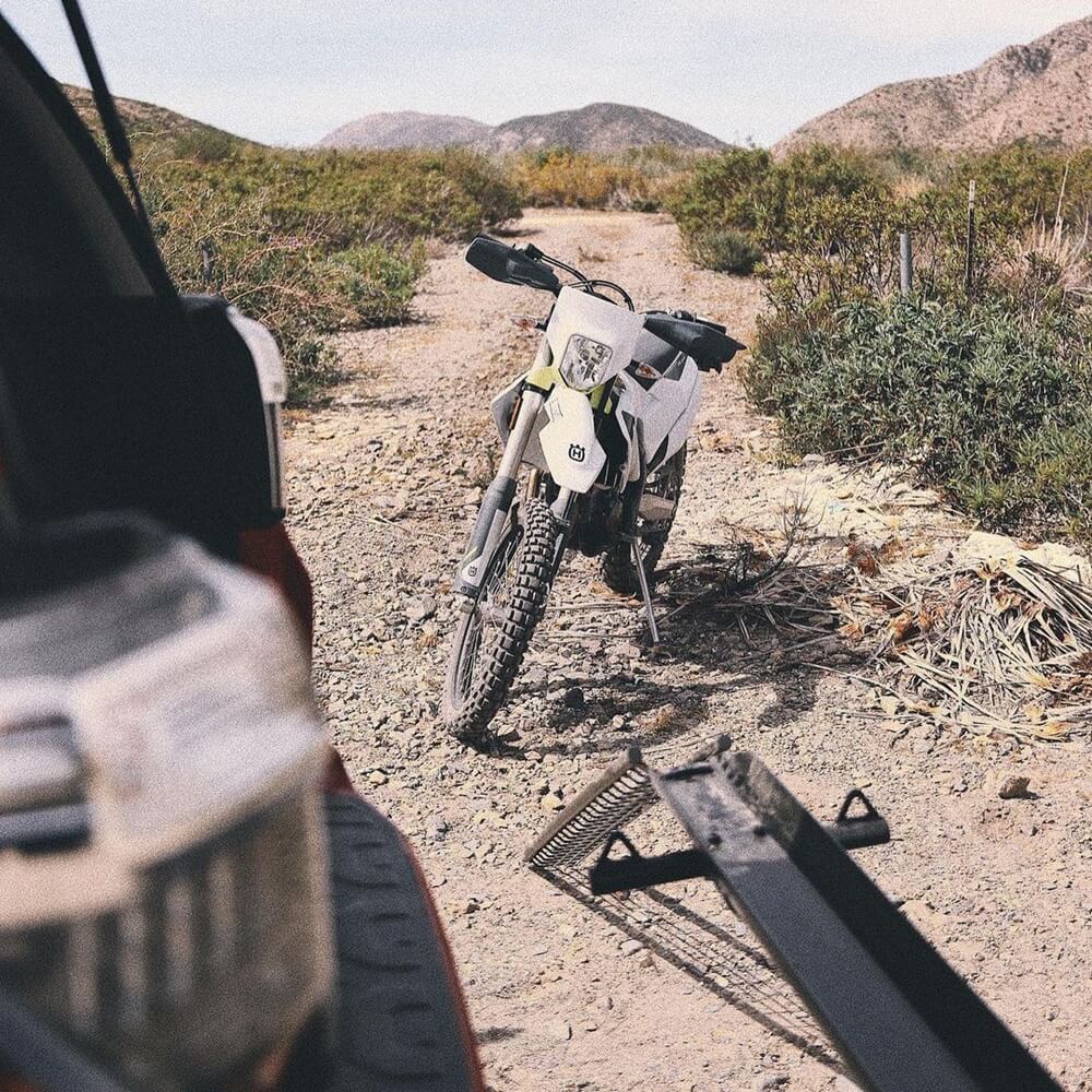 Husqvarna dirt bike being loaded onto a MotoTote M3 motorcycle hitch carrier in the desert, showcasing easy loading and secure off-road motorcycle transport.