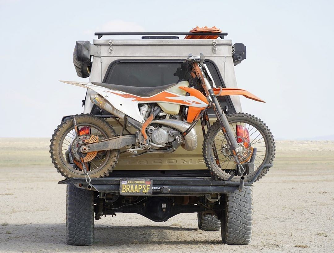 KTM dirt bike mounted on a MotoTote M3 motorcycle hitch carrier attached to an off-road truck in the desert, showcasing lightweight and secure dirt bike transport for adventure riding.