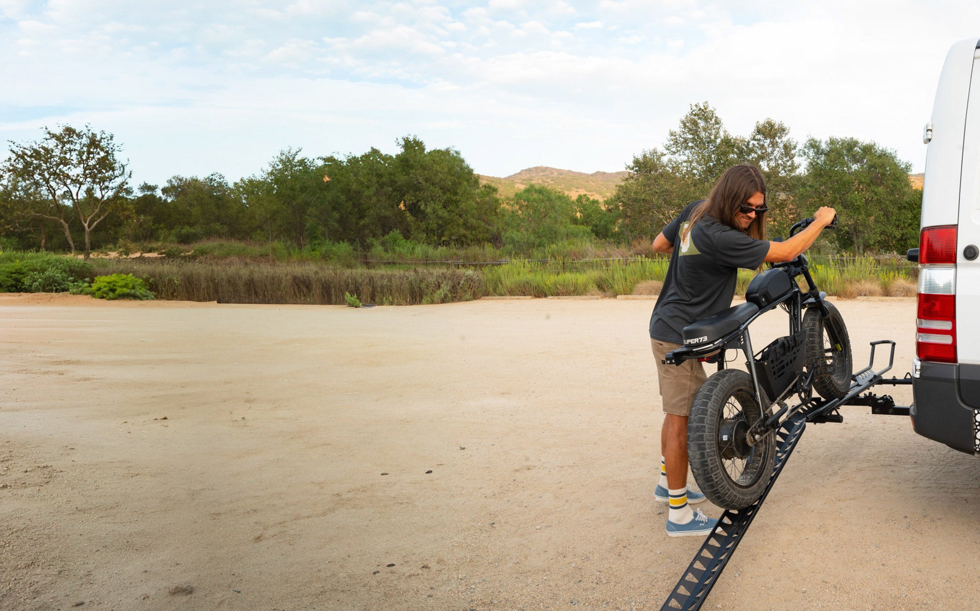 Rider loading an electric bike onto a MotoTote Mini electric bike carrier using a loading ramp accessory designed for easier heavy e-bike transport.