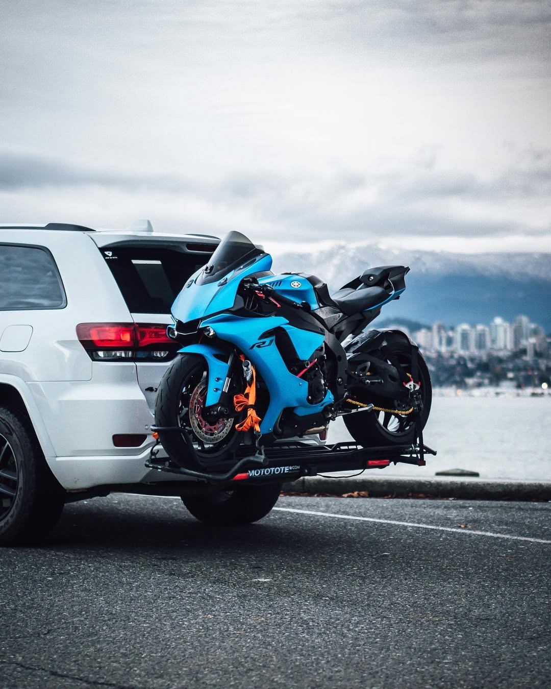 Blue Yamaha R9 sport motorcycle mounted on a MotoTote Sport motorcycle hitch carrier attached to a Jeep Grand Cherokee with snowy mountain scenery in the background.