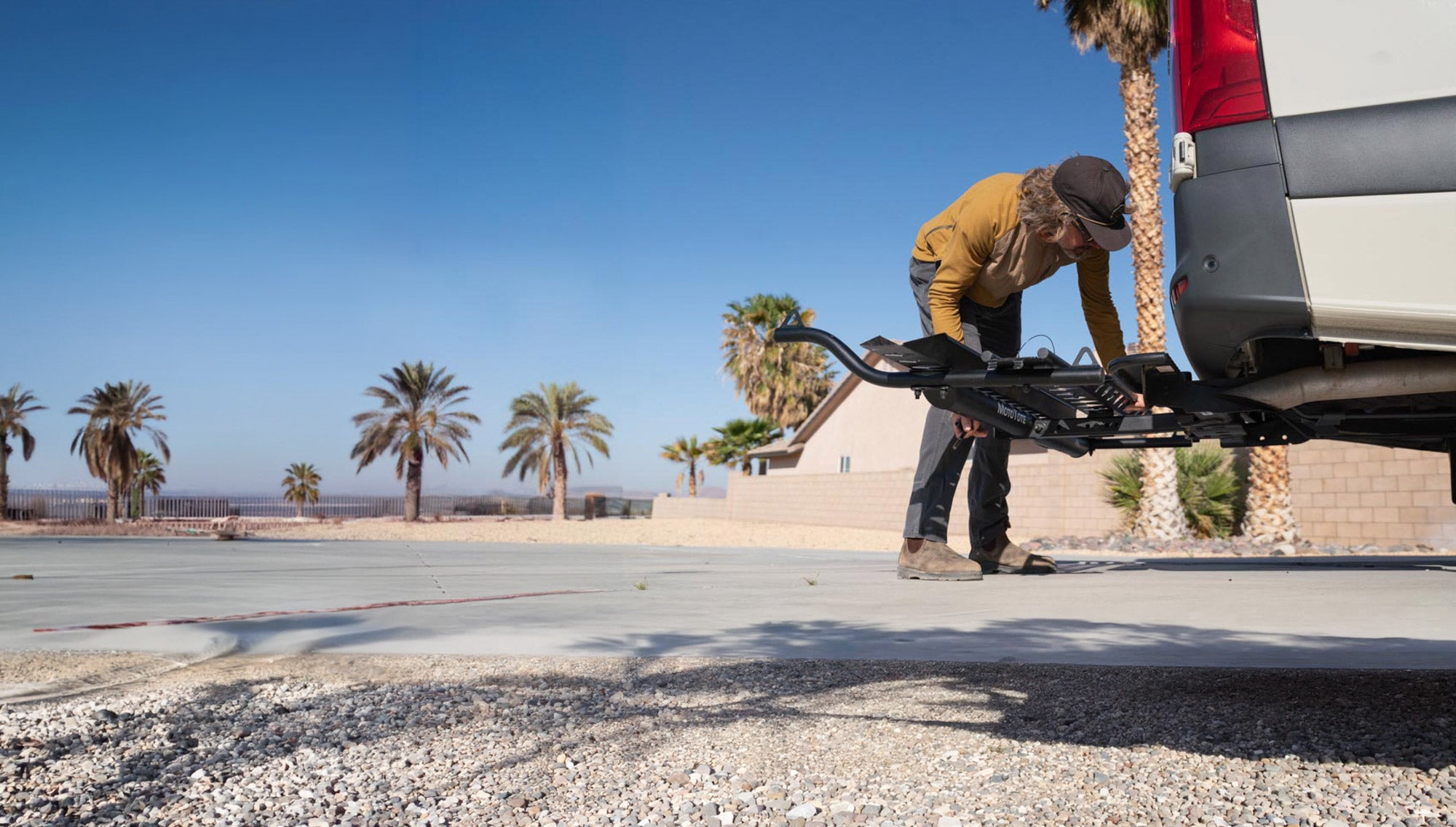Rider installing a MotoTote Max motorcycle carrier onto a Mercedes Sprinter van, showcasing replaceable parts and a serviceable design built to keep motorcycle carriers working for years of adventure travel.